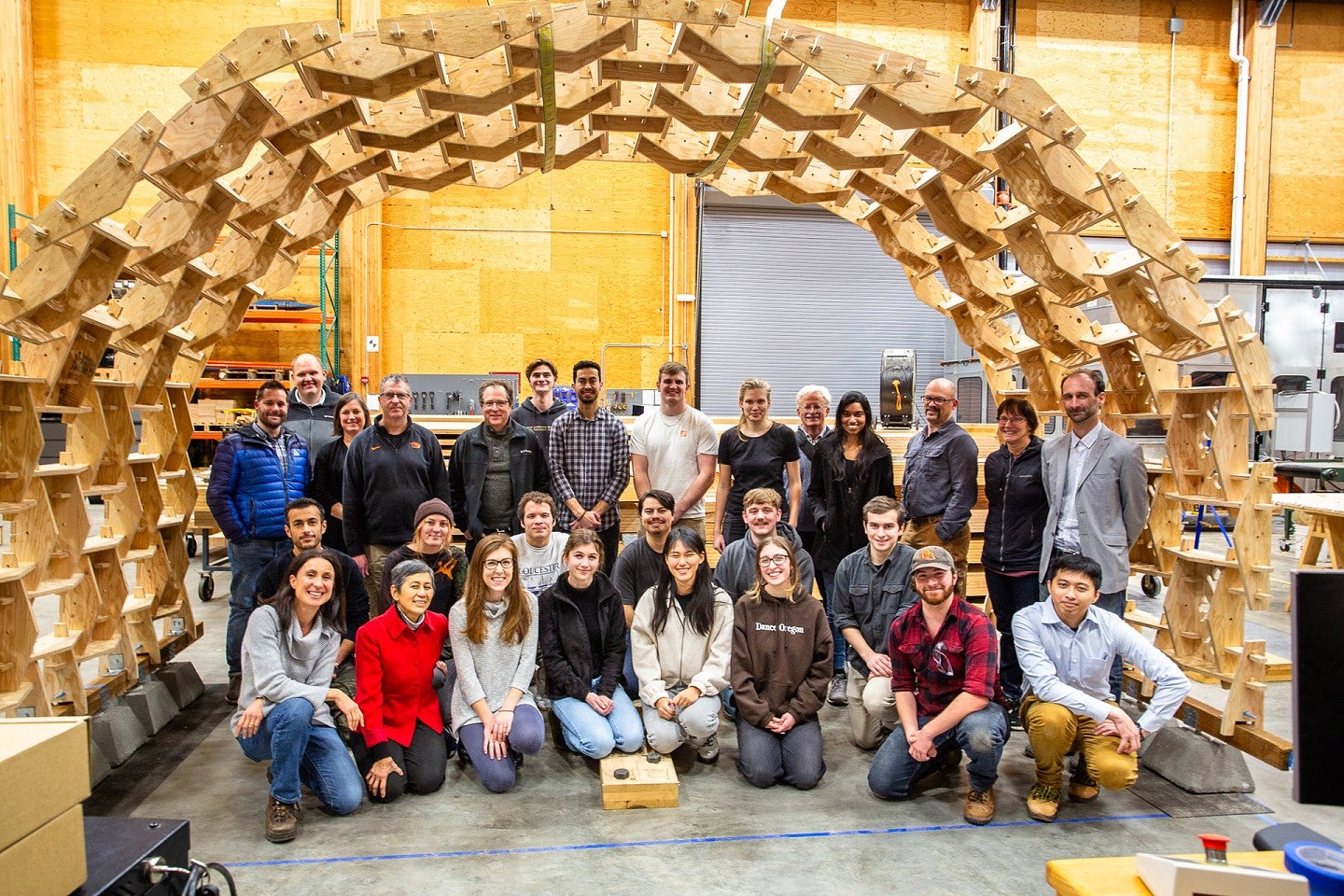 Students and faculty smile under a wooden archway they constructed themselves