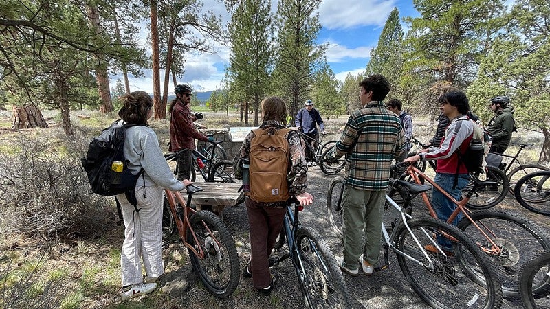 SCYP students, each with a bicycle, stand amongst trees around their instructor